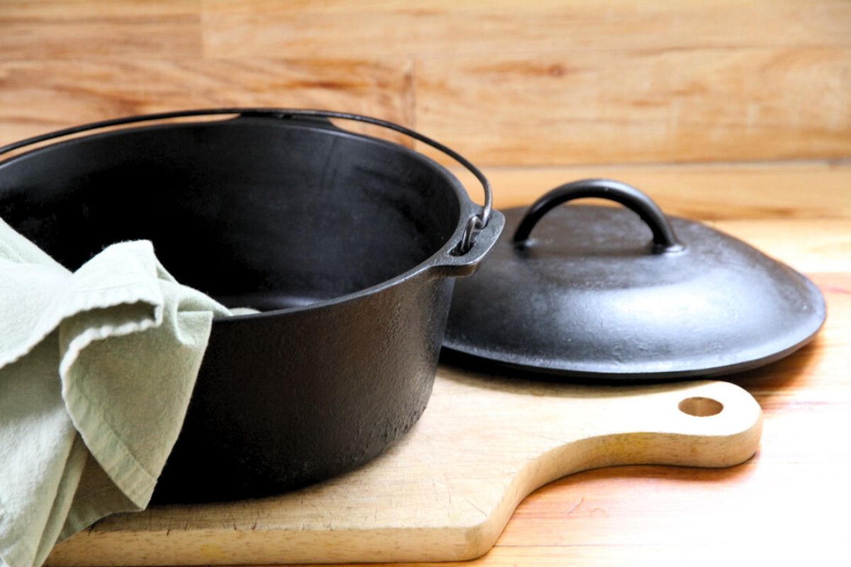 A black cast iron dutch oven and lid sitting on a wood cutting board and green tea towel.