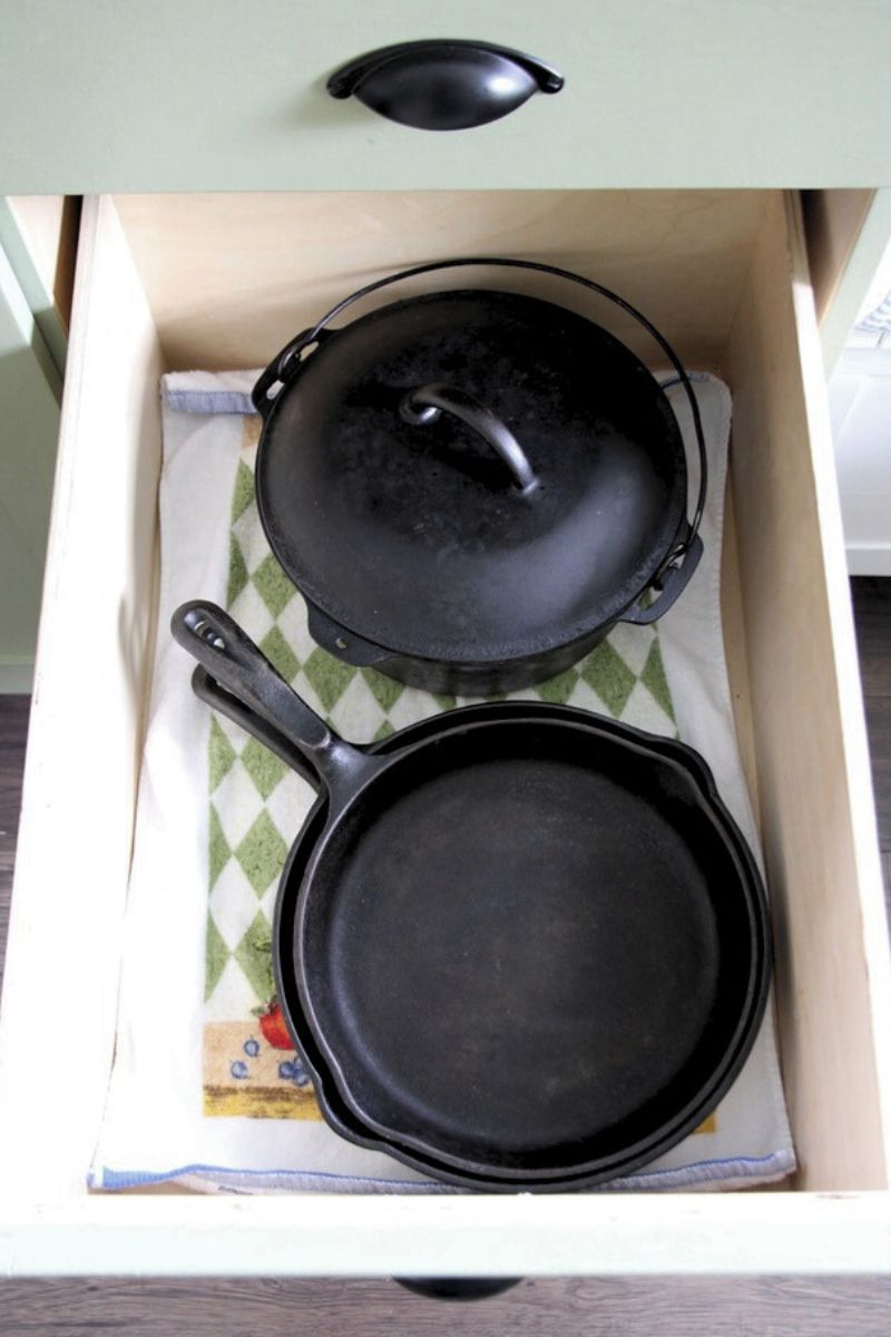 Cast iron dutch oven and cast iron pans stored in the bottom of a towel-lined drawer.
