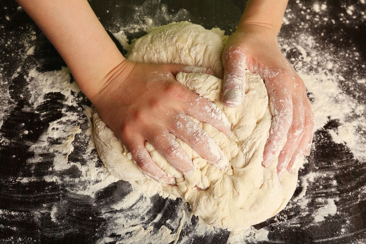 A woman's hands kneading dough on the table top.