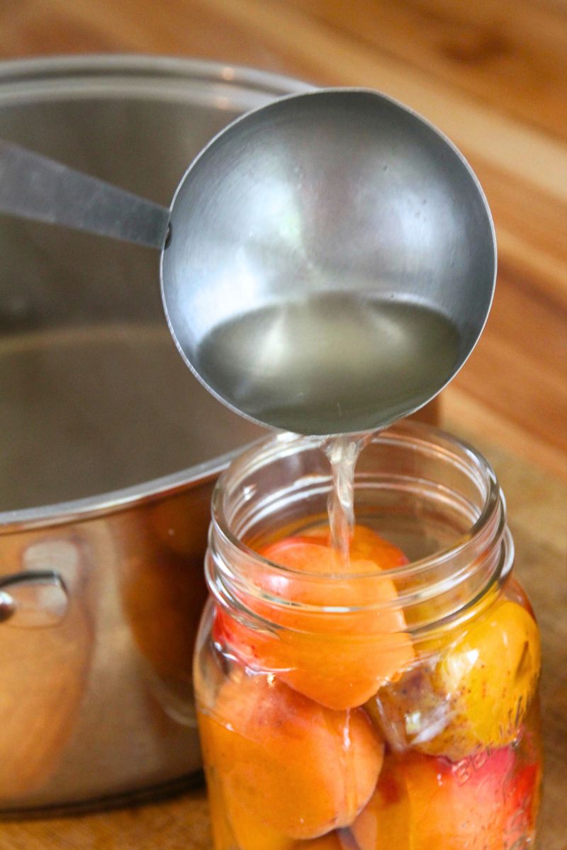 Ladling hot honey syrup into a jar of cold packed whole apricots.