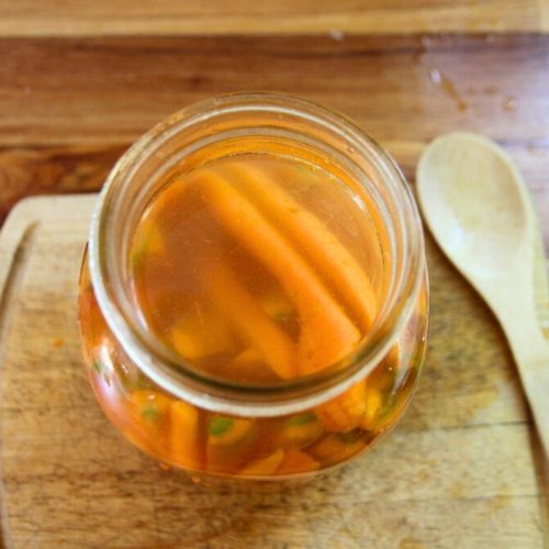 A glass jar filled with salt brine and carrot sticks.