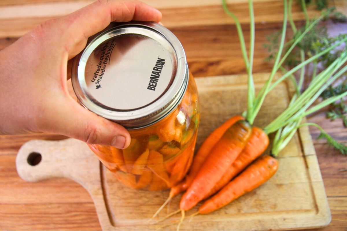 Adding a mason jar lid to a jar of fermenting carrot sticks.