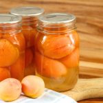 Three pint jars of freshly canned whole apricots on a wooden cutting board.