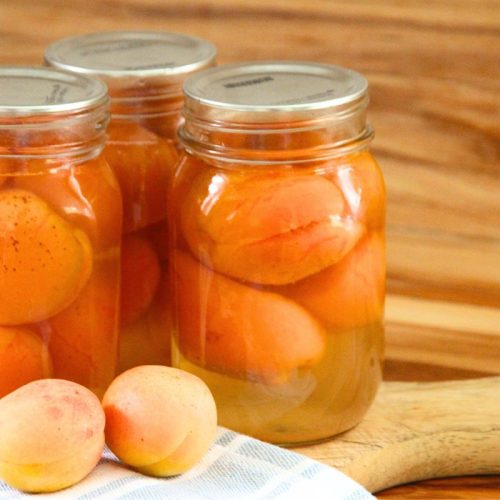 Three pint jars of freshly canned whole apricots on a wooden cutting board.
