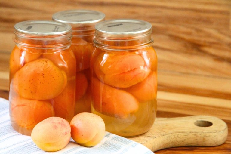 Three pint jars of freshly canned whole apricots on a wooden cutting board.
