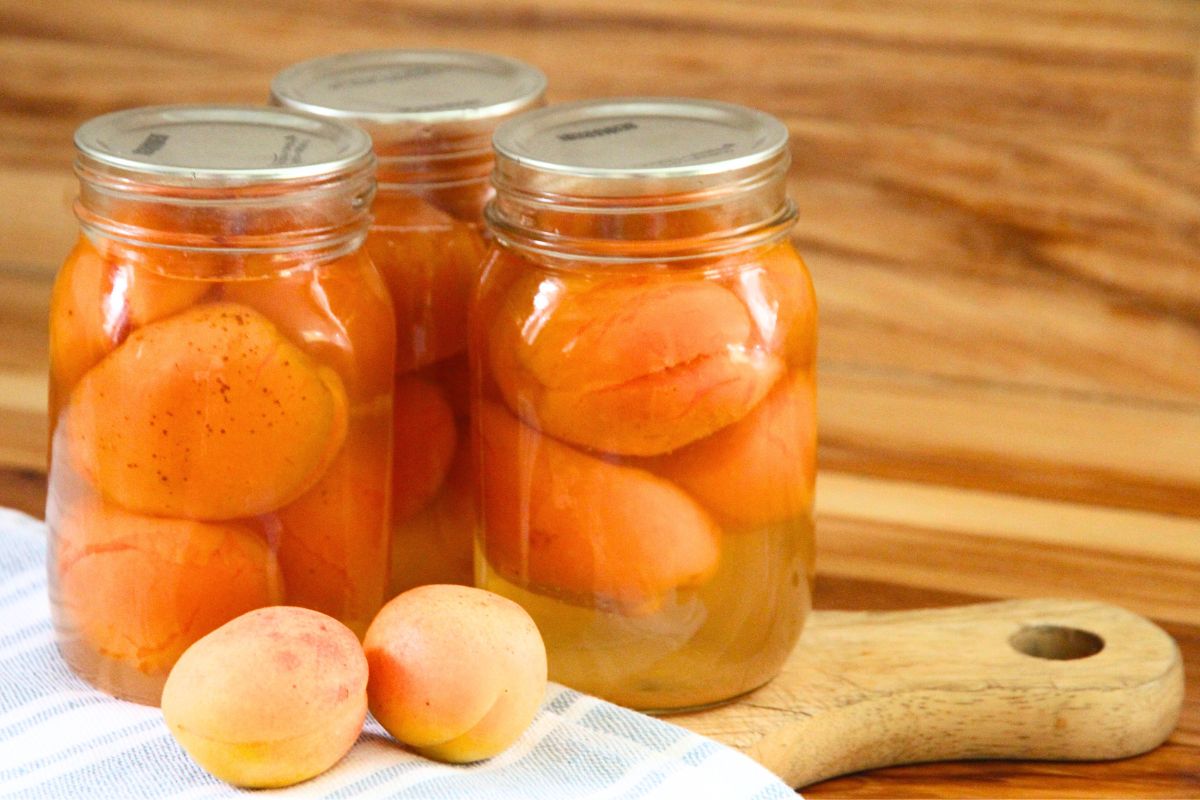 Three pint jars of freshly canned whole apricots on a wooden cutting board.