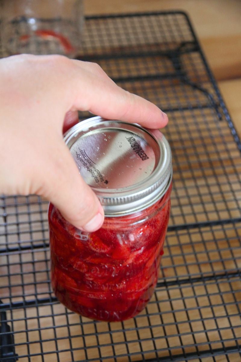 Adding a lid to a jar of strawberry sauce, so it can be preserved in the freezer. 