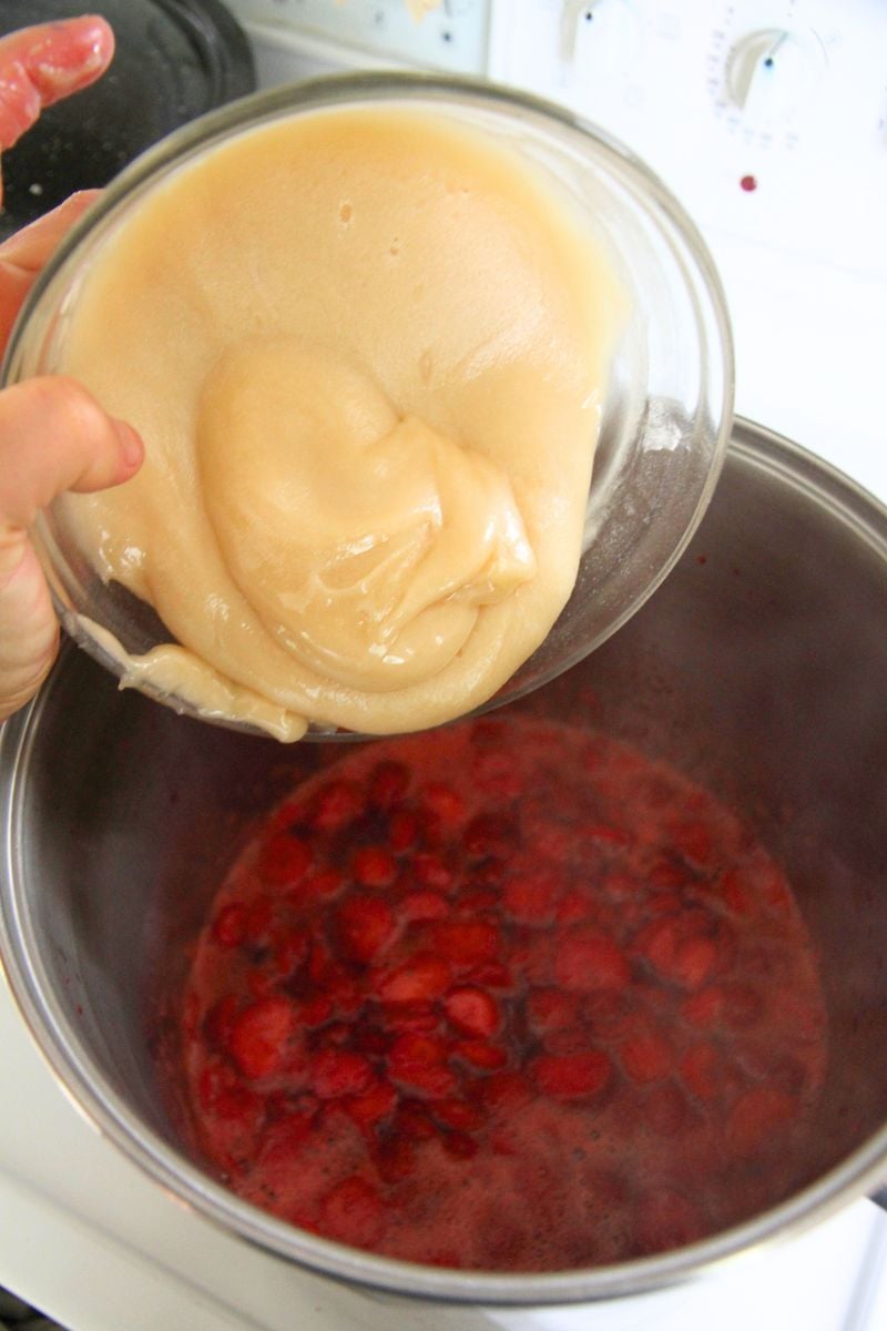 Adding honey and pectin to hot berry sauce on the stove top. 