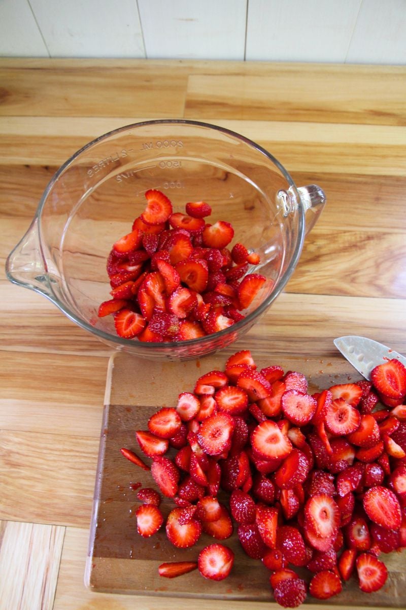 Slicing fresh strawberries into 1/4 inch rings and measuring sliced fruit in a measuring bowl. 