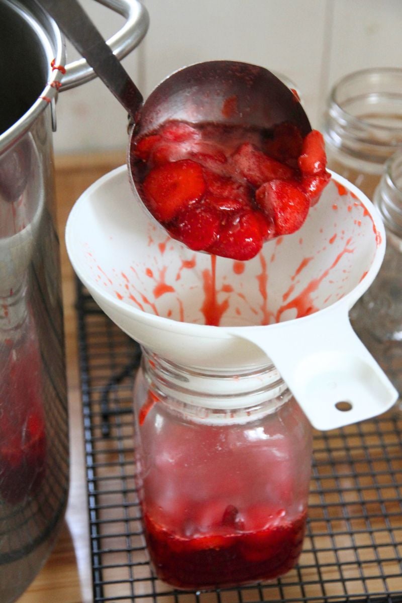 Ladling hot strawberry sauce into pint jars (500 ml) using a white funnel to keep things clean. 