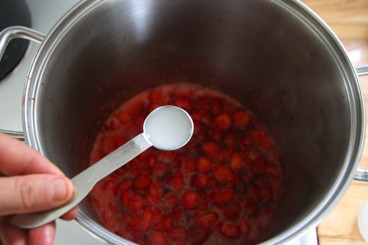 Measuring calcium water into cooking strawberries before adding honey and pectin. 