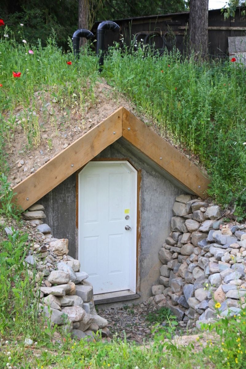 A concrete root cellar in a hillside with a white, exterior door.