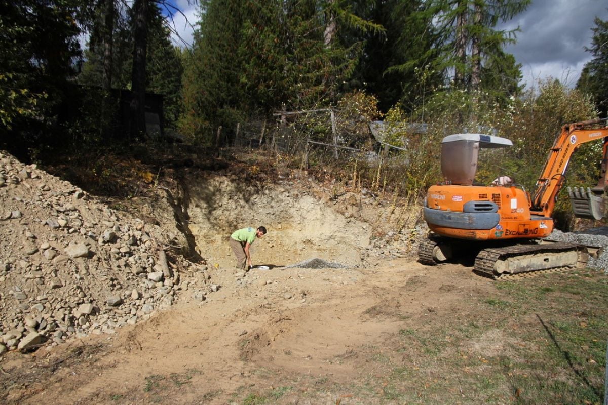 A man digging away a dirt bank with an orange excavator. 