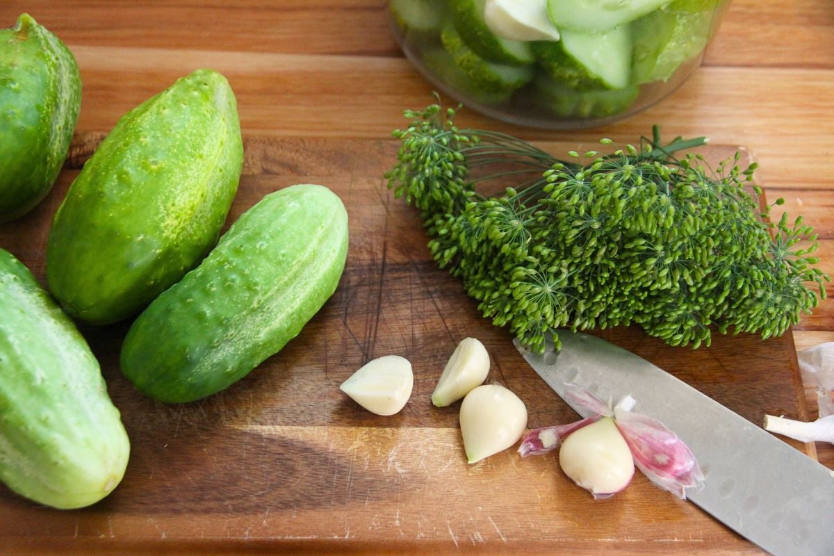 Cucumbers, garlic and fresh dill heads on a wooden cutting board.