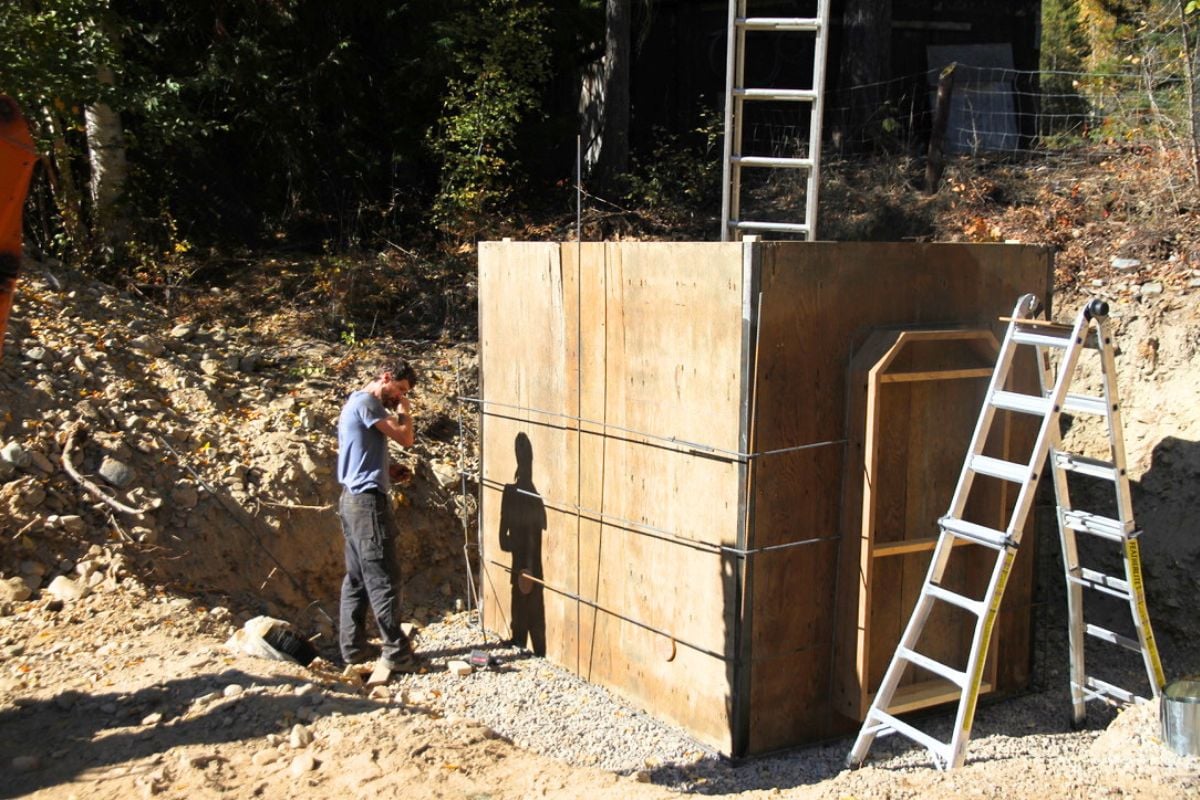 A man putting up interior plywood forms for the walls of the concrete root cellar. 