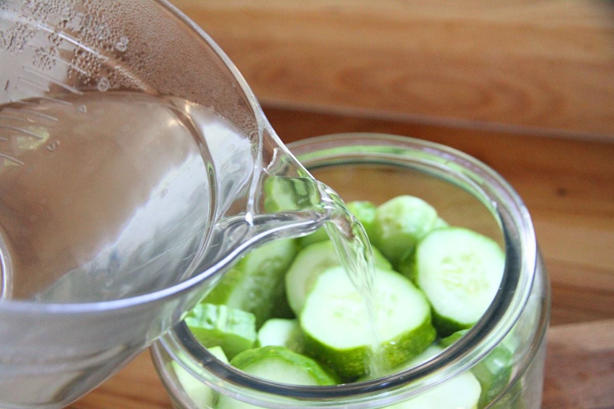 Pouring hot pickling brine over cucumbers to pickle them.