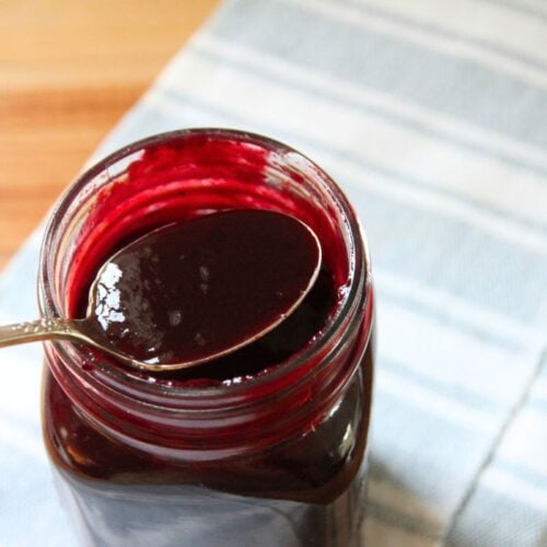 A jar of blackberry syrup with a spoon in the jar.