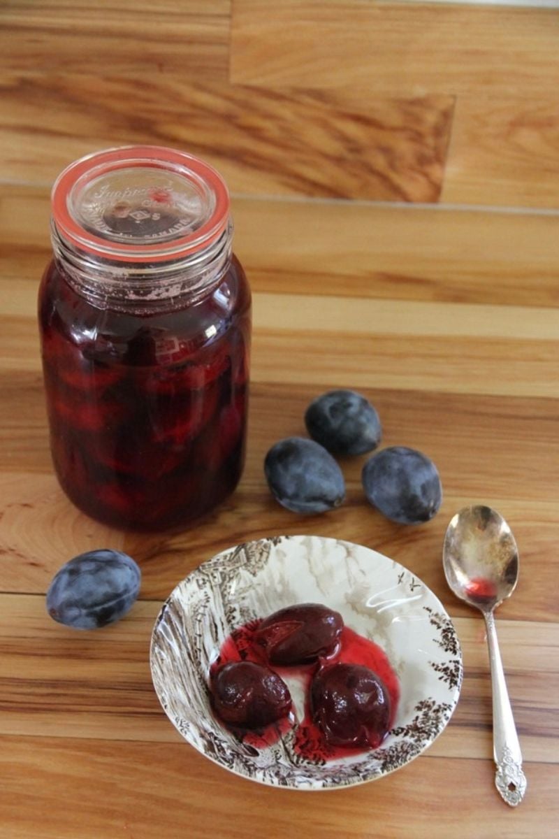 A jar of home canned plums, with a bowl of plums nearby.