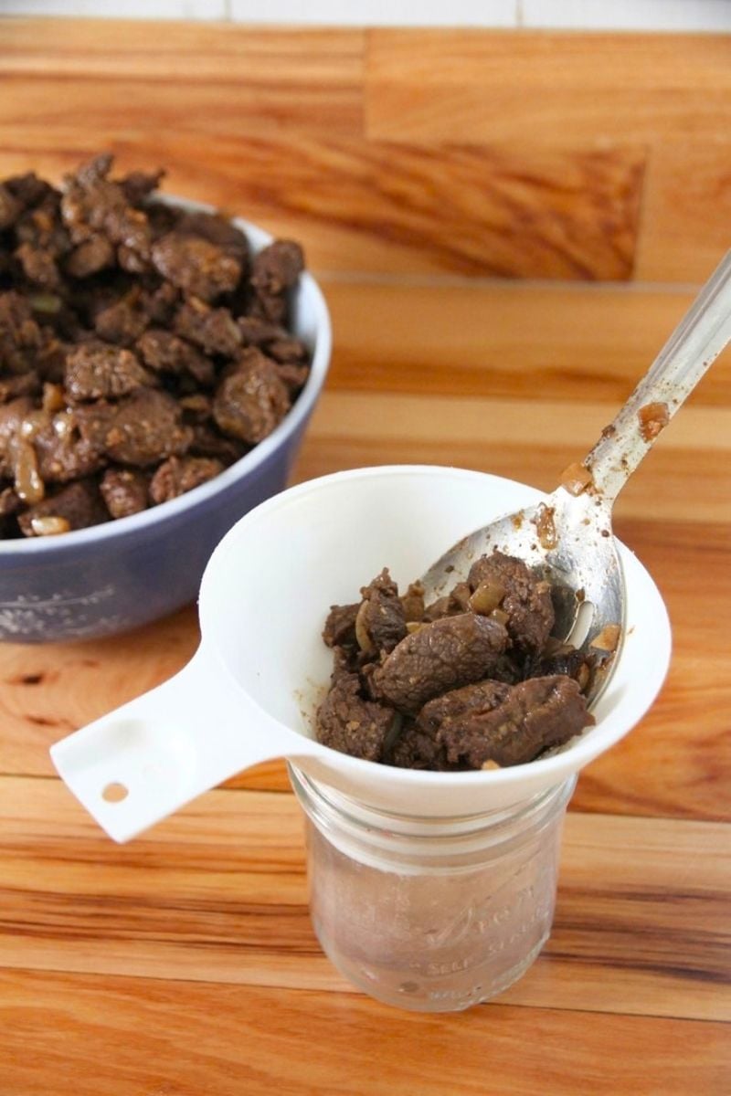 A jar with a white funnel resting on top, with bear meat being spooned into the funnel and jar.