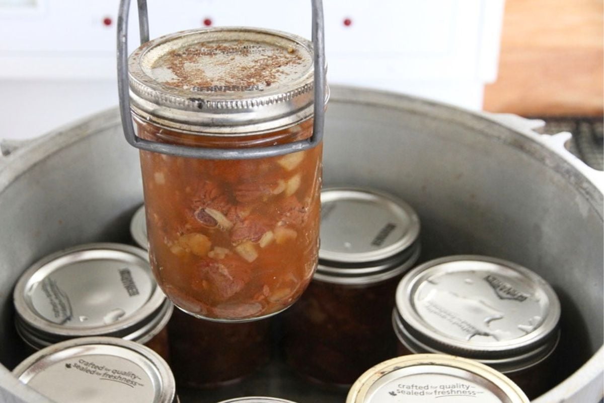 Lifting a canned jar of bear meat from the canner with a jar lifter.