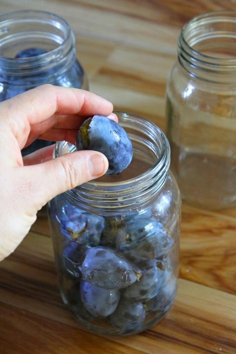 Filling a jar with whole, pitted purple Italian plums.
