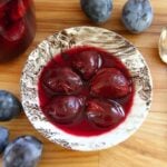 A bowl of 5, whole canned plums in delicious, purple red juice.