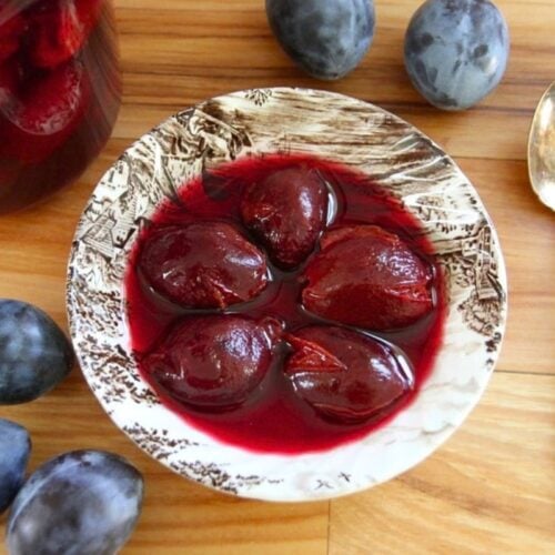 A bowl of 5, whole canned plums in delicious, purple red juice.