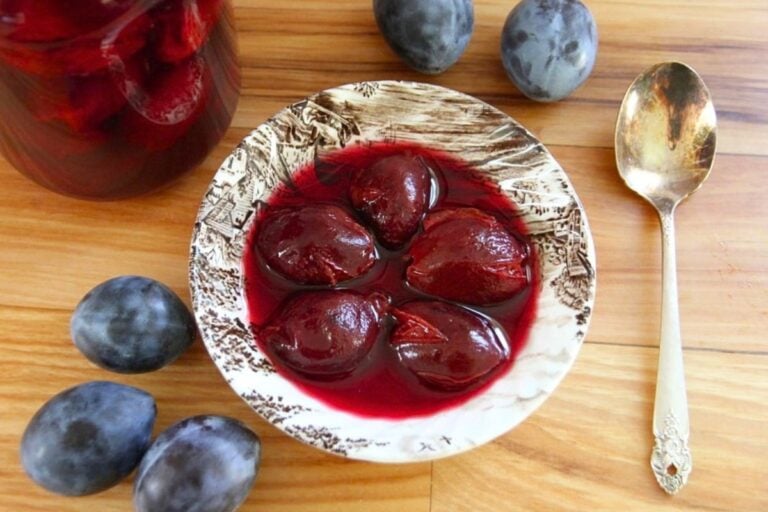 A bowl of 5, whole canned plums in delicious, purple red juice.