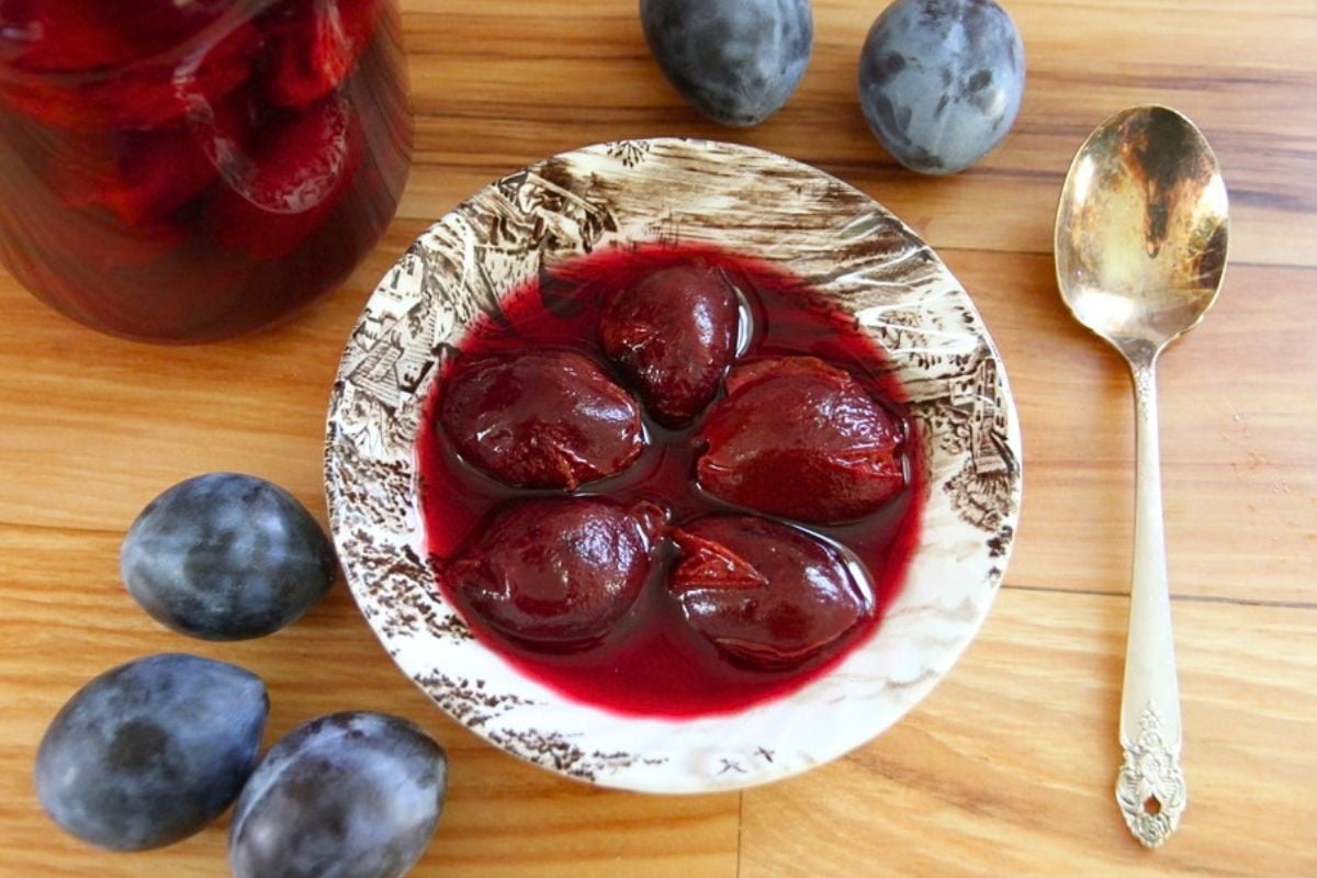 A bowl of 5, whole canned plums in delicious, purple red juice.