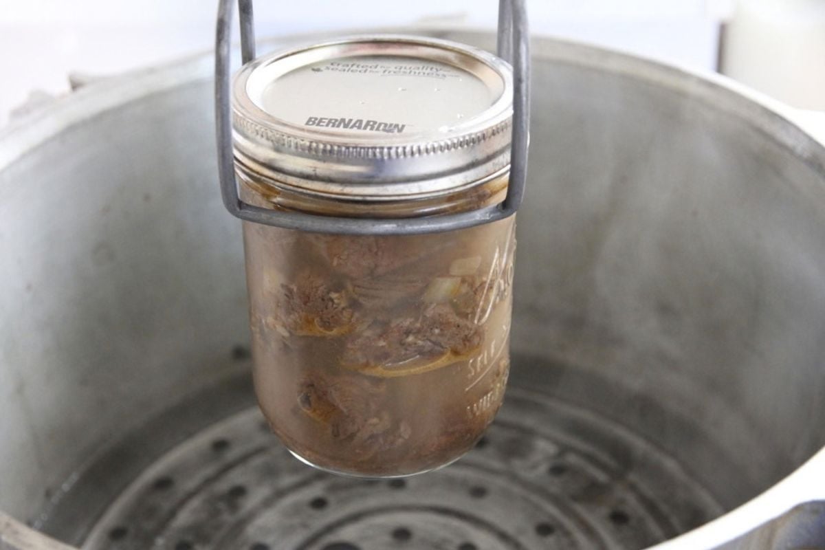 A jar of bear meat being set in a pressure canner with a jar lifter.
